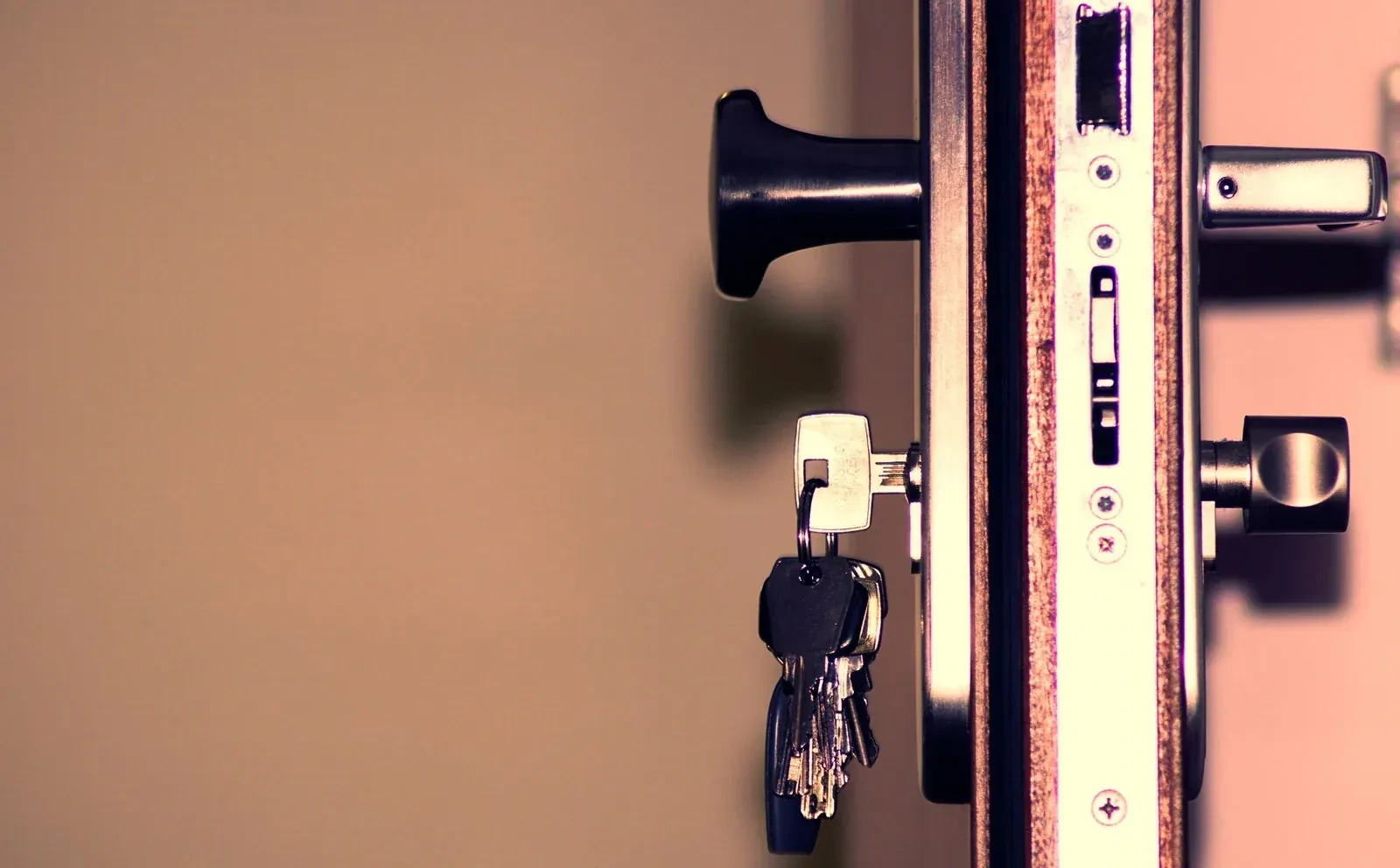 Bunch of keys hanging from a key in a door lock, beside a black knob and the door's metal edge plate.